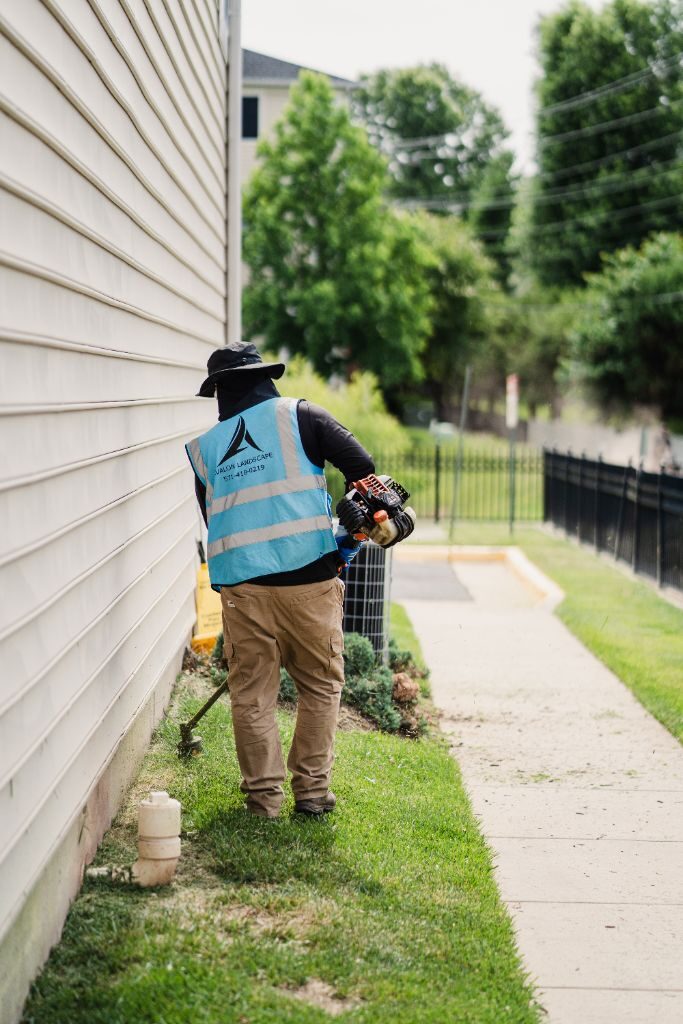 Avalon crew member trimming along a building foundation and sidewalk