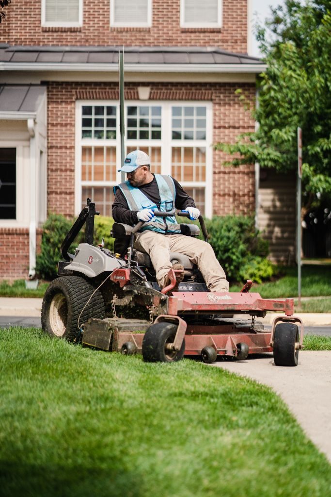 Avalon crew member on a zero-turn mower in front of a townhome community