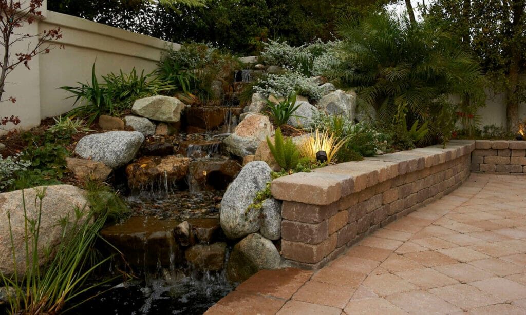 Terraced stone retaining wall holding back a sloped, planted backyard