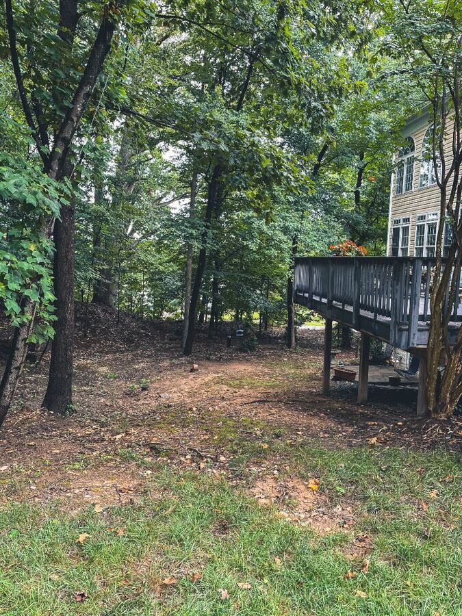 Before: bare dirt path under a deck with no grass or drainage established