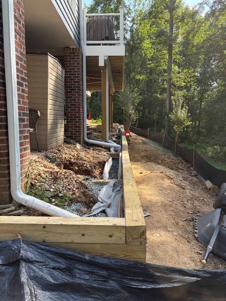 Avalon crew building a timber retaining wall along a sloped side yard, with drainage gravel and pipe installed behind it